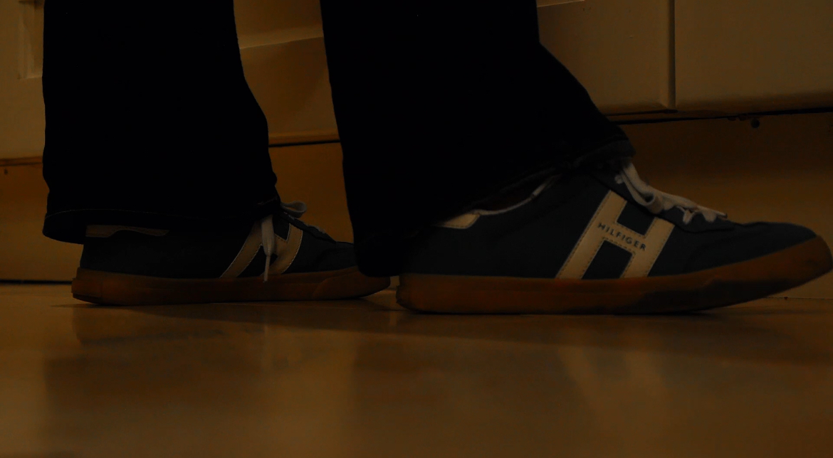 Two navy trainers walking across a lit corridor floor