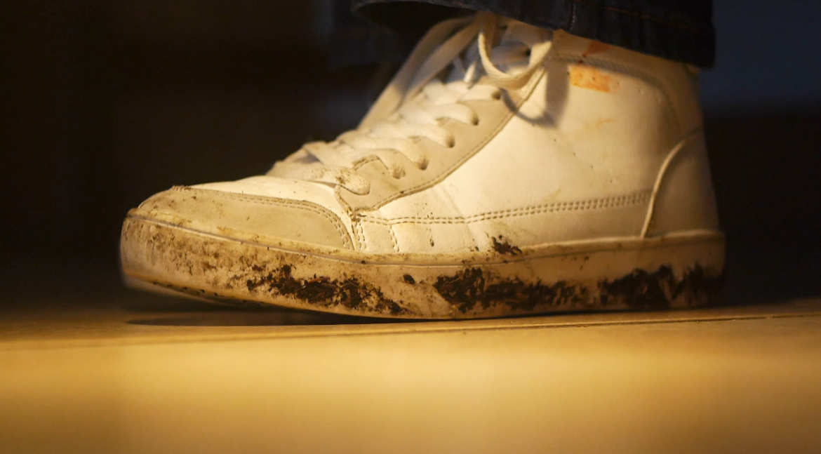 Low-angle close-up of a mud-caked white high-top sneaker on a wooden floor